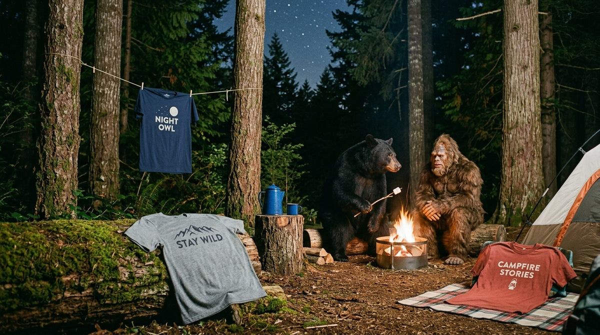 WrongTrails Campfire and Cryptids collection banner featuring Sasquatch and a black bear roasting marshmallows by a night campsite fire, displaying Stay Wild, Campfire Stories, and Night Owl graphic tees.